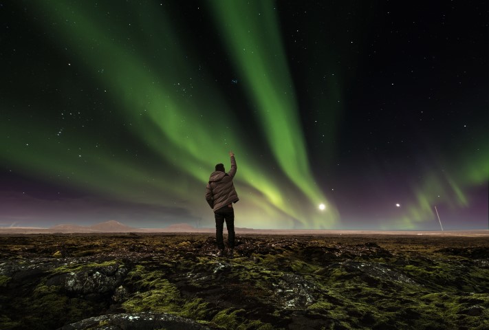 Man standing under the Northern Lights in Iceland Man standing under the Northern Lights in Iceland